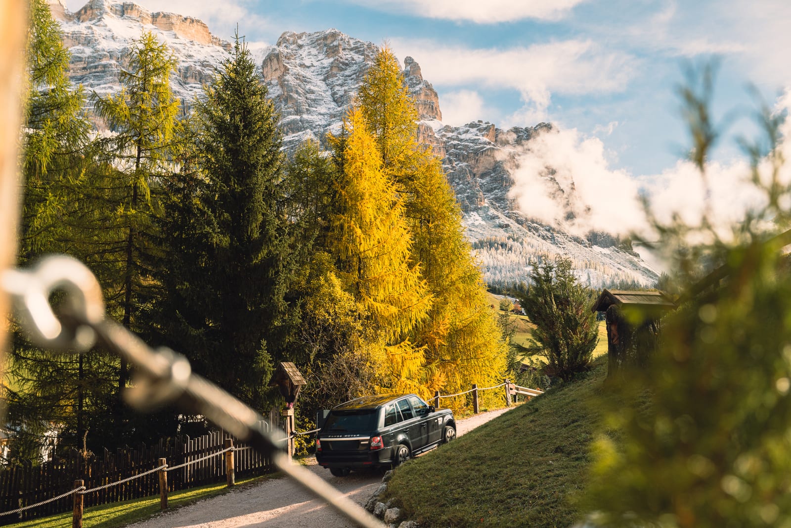 Yellow autumn larches and snowy peaks; a car climbs a mountain road. Photograph by Luca Canins.