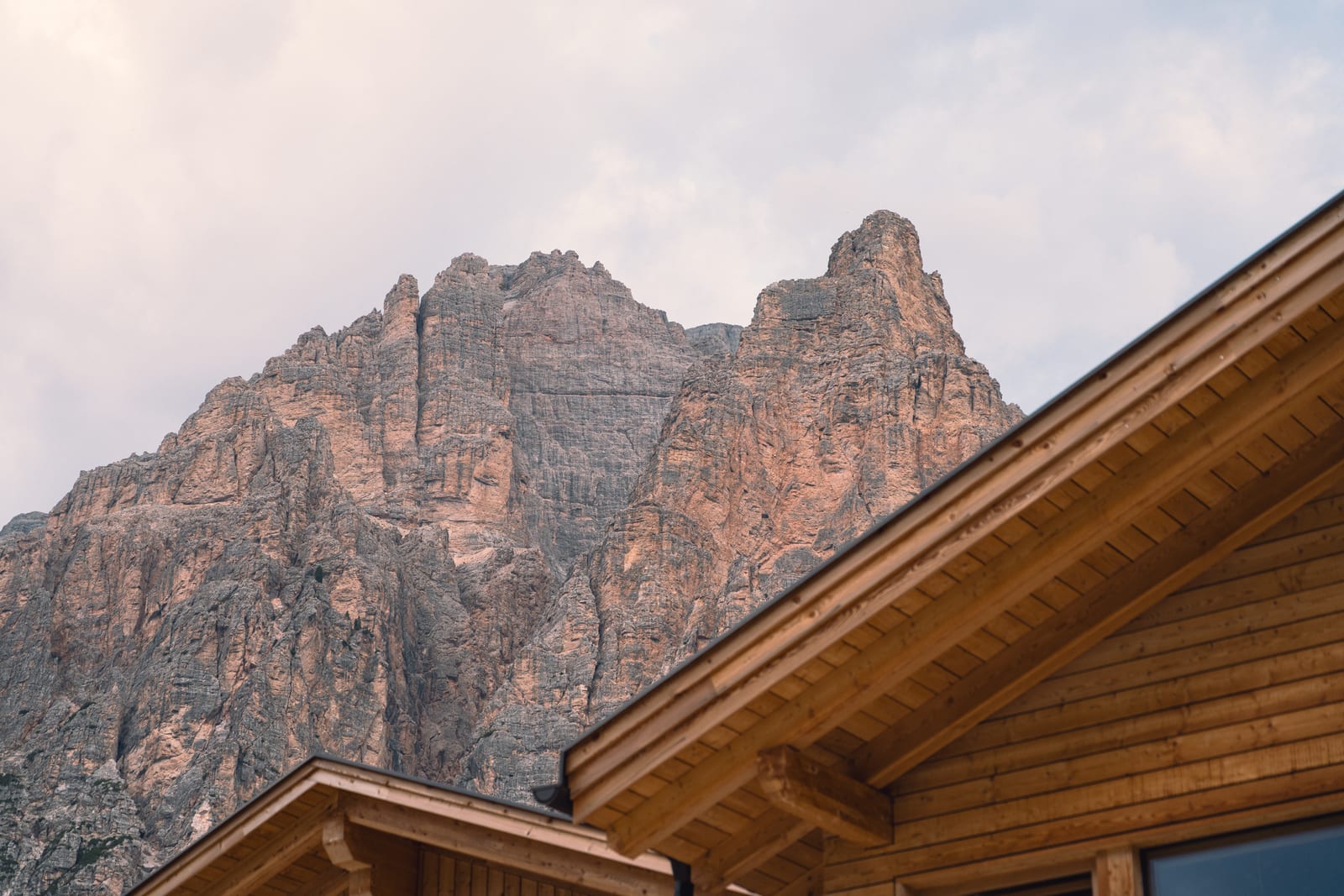 A chalet’s wooden roof against a rock face, in warm light. Photograph by Luca Canins.